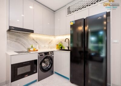Modernná kuchyňa s bielymi skriňami, práčkou a chladničkou v apartmáne SIAMIQ, Thajsko.