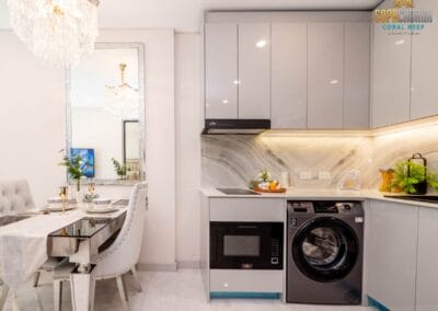 Moderná kuchyňa v apartmáne SIAMIQ, štýlové vybavenie, biele skriňky, práčka a mikrovlnka.