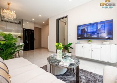 Modern living room with white furniture, flat-screen TV, and decorative plants.
