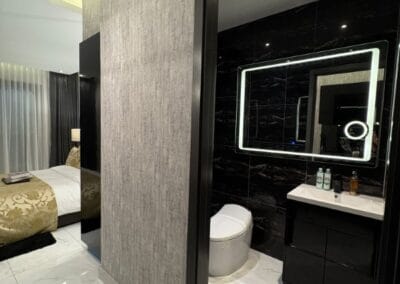 Modern hotel bathroom with black and white decor and illuminated mirror.
